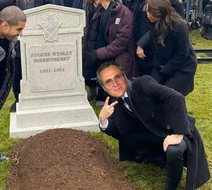 Person with the head of Star Trek producer Rick Berman joyously posing over a grave with a tombstone inscribed with the words "EUGENE WESLEY RODDENBERRY 1921-1991"