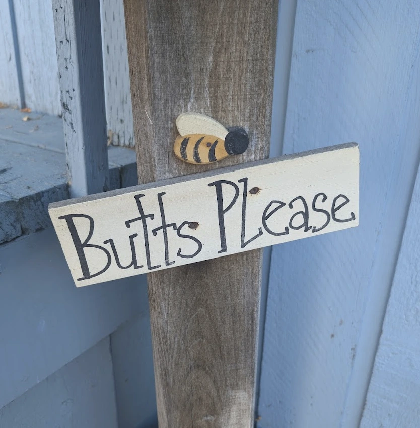 A small wooden sign with a bumblebee asking for butts. Also - Rule.